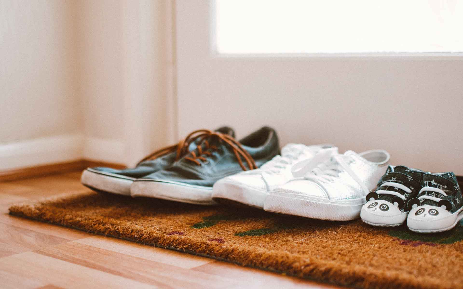 Shoes of various sizes on a doormat, including adult sneakers and children's shoes, symbolizing family and home life.