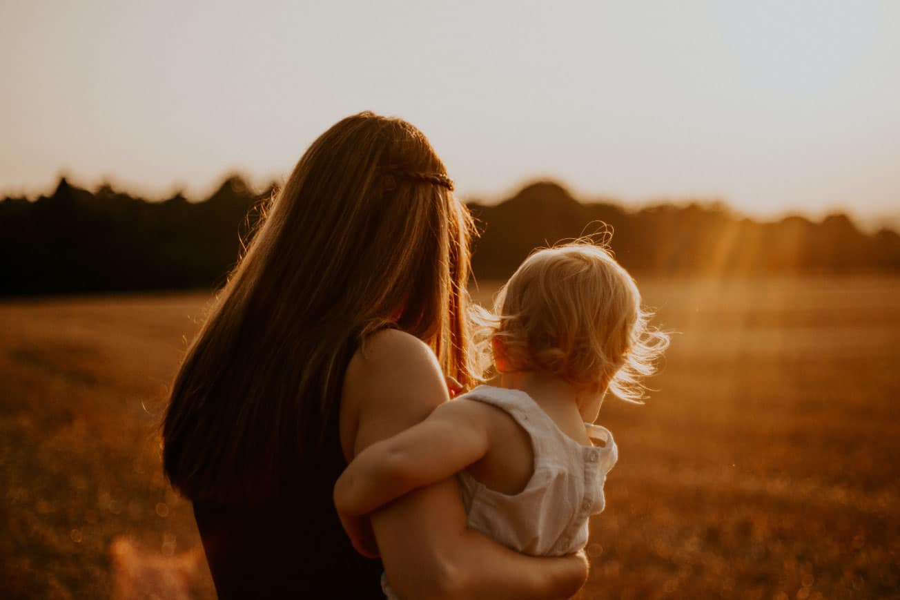 Mother holding child in a sunlit field, symbolizing family and nurturing relationships in a serene outdoor setting.