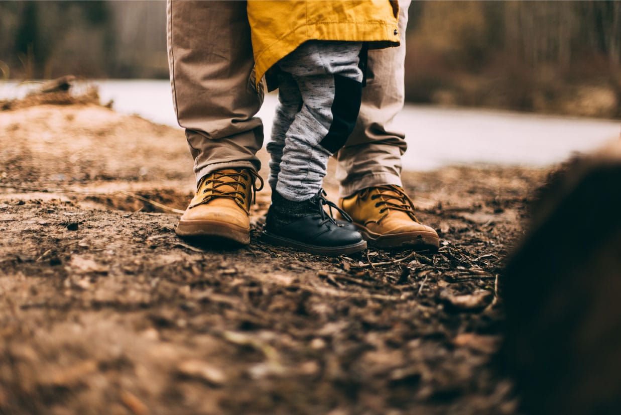 Adult and child standing together on dirt path, showcasing sturdy footwear, symbolizing family support and outdoor adventures.