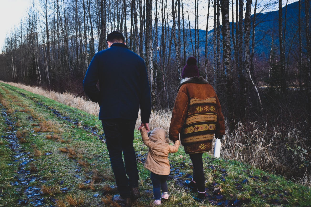 Family walking together on a grassy path, with a child holding hands with parents, surrounded by trees and mountains, evoking a sense of home and togetherness in the context of home buying and mortgage processes.
