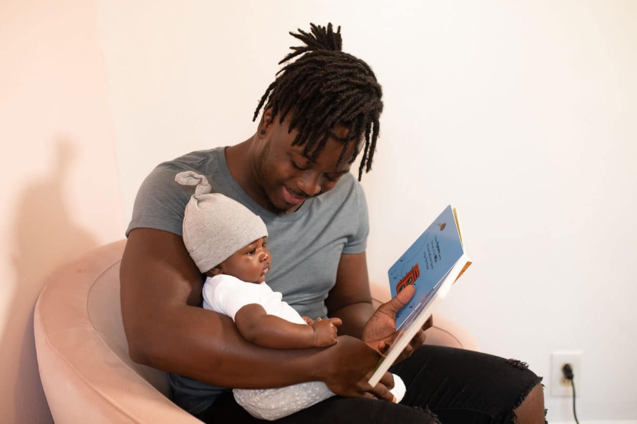 Father reading a children's book to a baby in a cozy setting, emphasizing family bonding and early literacy.