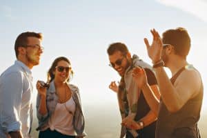 Group of four friends enjoying a lively conversation outdoors, smiling and gesturing against a clear sky, reflecting a sense of camaraderie and happiness.